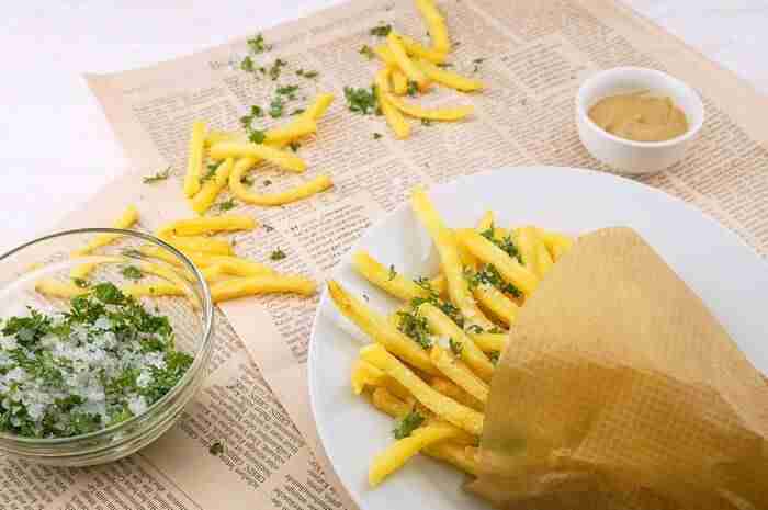 French fries inside a paper cone sitting on a plate with salt and seasoning on them